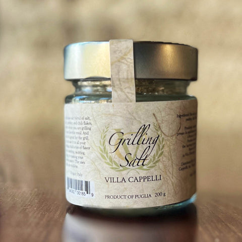 A jar of Villa Cappelli Grilling Salt, placed on a wooden surface with a focus on its label, displaying product details.
