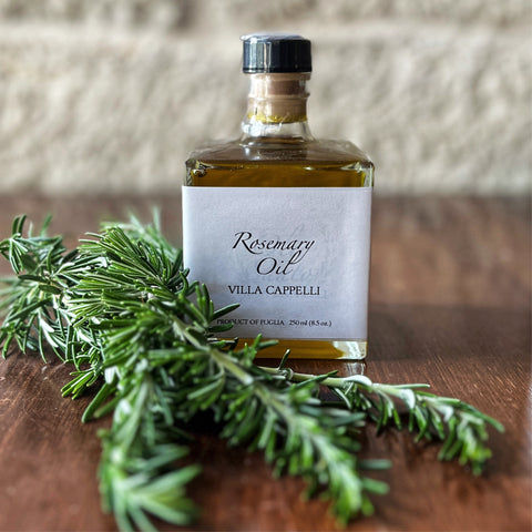 A bottle of Villa Cappelli Rosemary Oil with fresh rosemary sprigs on a wooden surface.