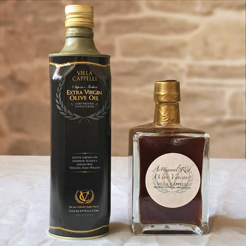 Two bottles on a table: one tall, green bottle labeled "Villa Cappelli Extra Virgin Olive Oil" and one square, amber bottle of "Hand-Crafted Red Wine Vinegar Villa Cappelli.