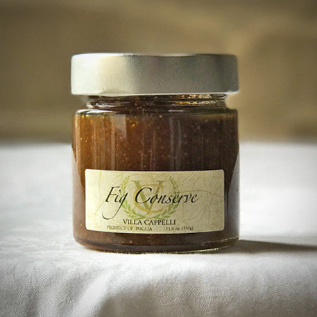 A glass jar of Villa Cappelli Italian Fig Conserve on a table, labeled "Villa Cappelli, product of Puglia," against a lightly blurred background.