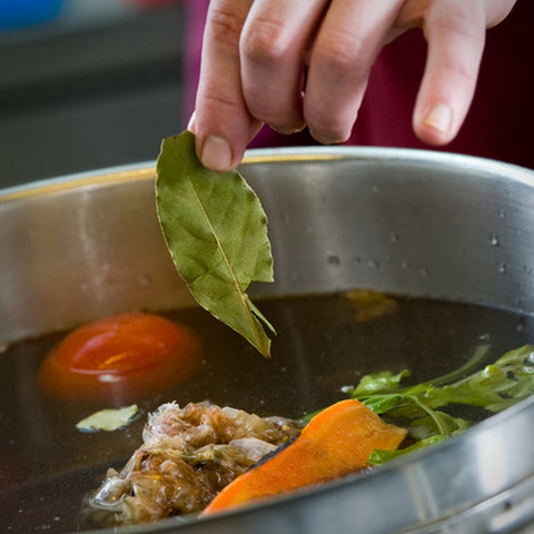 A person removing a leaf of Villa Cappelli Italian Bay Leaves from a pot of food.