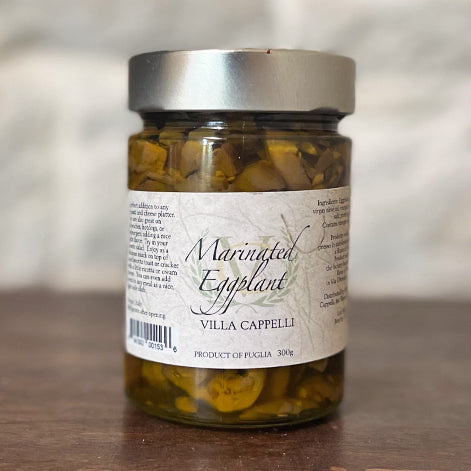 A jar of Villa Cappelli Marinated Eggplant labeled "Villa Capelli, product of Puglia, 300g" placed against a blurred wooden backdrop is perfect for antipasti.