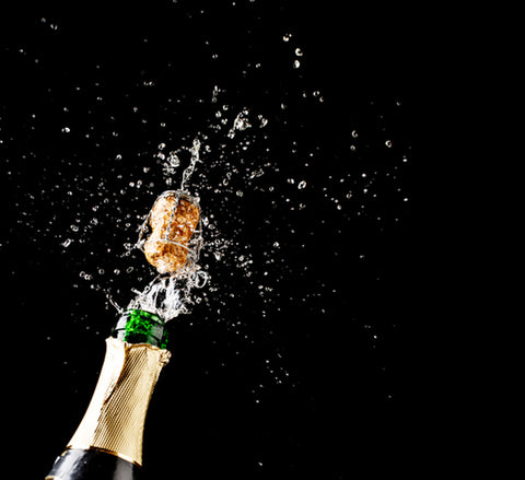 Villa Cappelli Prosecco Vinegar cork popping off a bottle with bubbles and spray against a dark background.