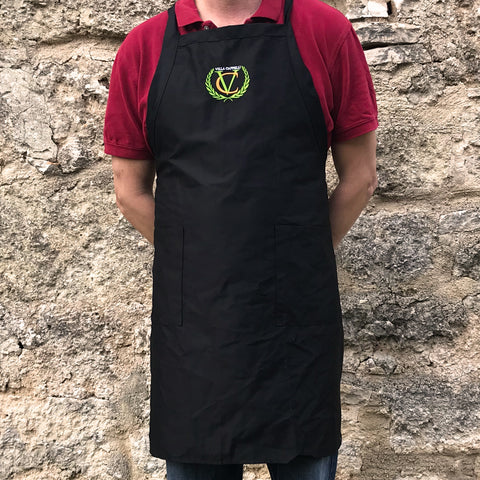 A man wearing a Villa Cappelli cross-back apron standing in front of a stone wall.