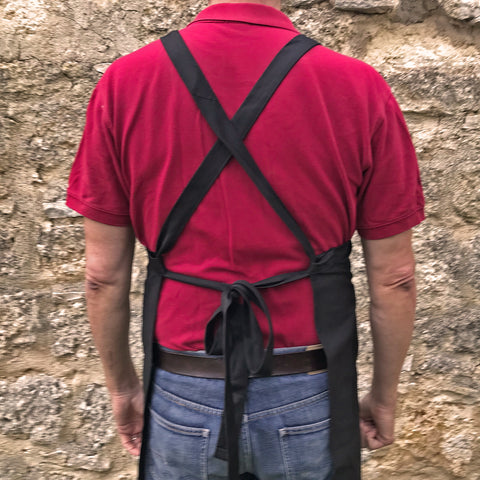 A man wearing a Cross-Back Villa Cappelli apron standing in front of a stone wall.