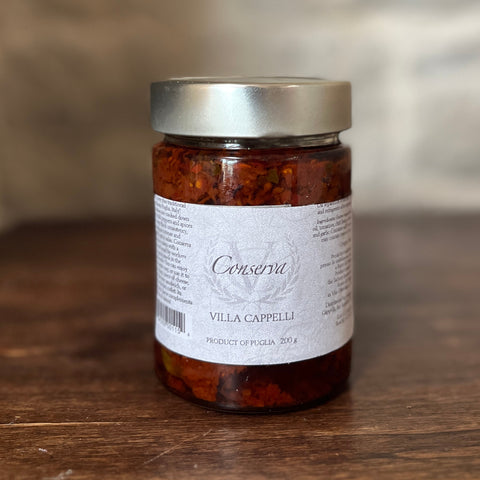 A traditional treat from Puglia, a jar of Villa Cappelli Tomato Conserva sits on a wooden table.