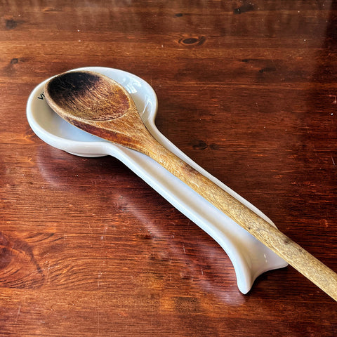 A wooden spoon rests on the Pausa Perfetta spoon rest by Villa Cappelli, handcrafted in Puglia, displayed on a brown wooden table.