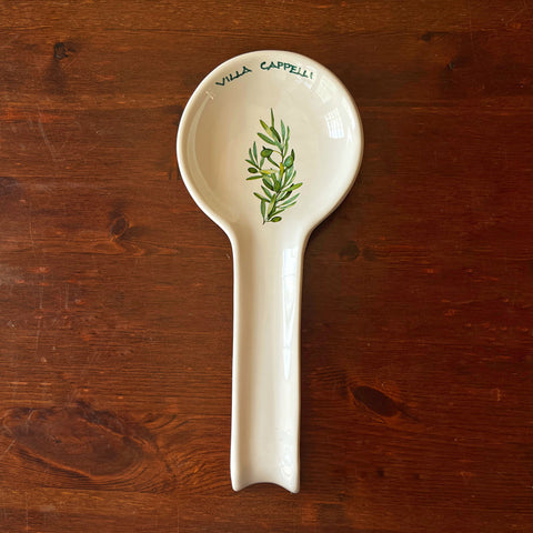 The Pausa Perfetta by Villa Cappelli is a handcrafted white ceramic spoon rest from Puglia, featuring a green olive branch design and logo—perfect for Italian cooking enthusiasts.
