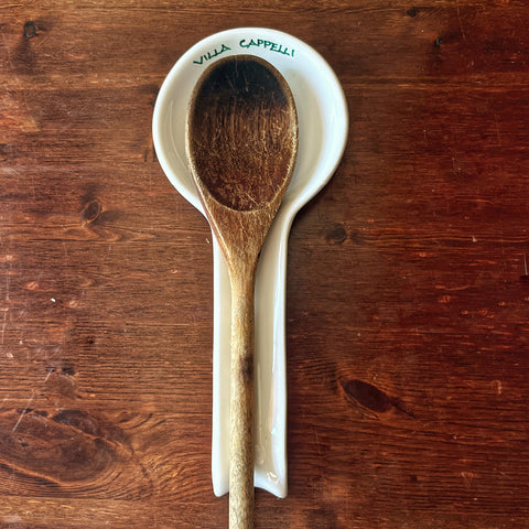 A wooden spoon rests on the Pausa Perfetta spoon rest by Villa Cappelli, handcrafted in Puglia and set on a wooden tabletop.