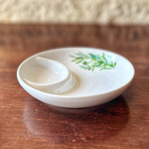 The Villa Cappelli Spuntino Server is a handcrafted ceramic white divided dish with a green leafy design on one section, bringing Mediterranean charm to your table, especially when set on wood.