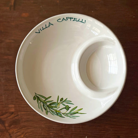 The Villa Cappelli Spuntino Server is a handcrafted white ceramic plate with a divider, featuring green olive branch artwork and "Villa Cappelli" on the rim—perfect for adding Mediterranean charm to your table.