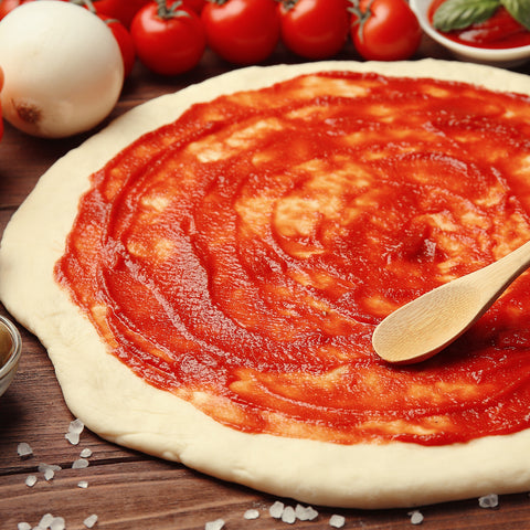 A pizza topped with Villa Cappelli passata (strained tomatoes) is sitting on a wooden table.