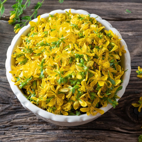 Yellow flowers, such as Villa Cappelli St. John's Wort Oil, decoratively arranged in a bowl on a wooden table.
