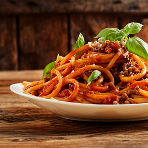 Spaghetti with Villa Cappelli Spicy Sun-Dried Tomato Spread on a wooden table.