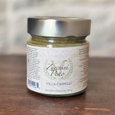 A jar of Villa Cappelli Zucchini Pesto pasta sauce on a wooden table.
